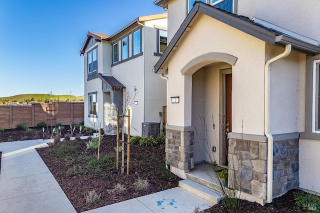 doorway to property featuring central AC unit, fence, stone siding, and stucco siding