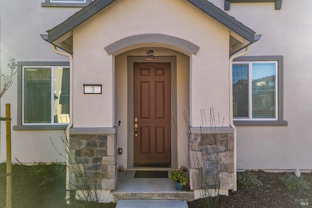 view of exterior entry featuring stucco siding and stone siding