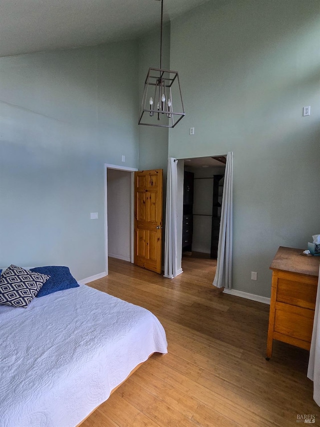 bedroom with high vaulted ceiling, an inviting chandelier, baseboards, and wood finished floors