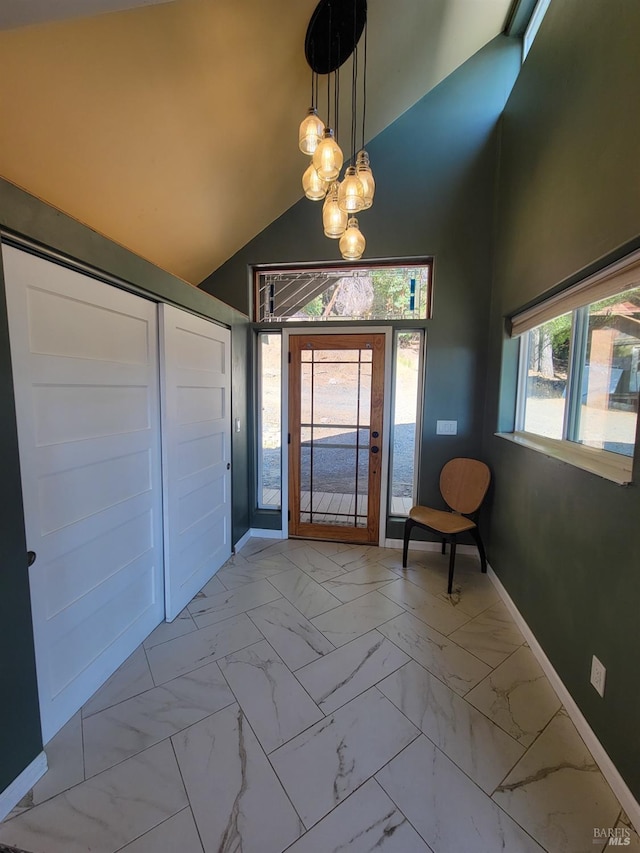 foyer entrance with high vaulted ceiling, marble finish floor, baseboards, and an inviting chandelier