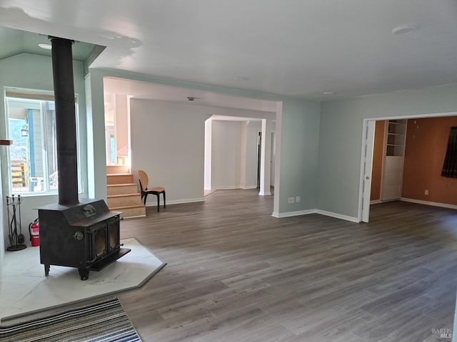 unfurnished living room featuring a wood stove, baseboards, and wood finished floors