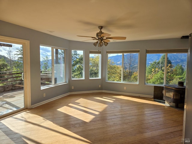 unfurnished sunroom featuring a wood stove and a ceiling fan