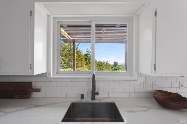 kitchen with tasteful backsplash, white cabinetry, light stone counters, and a sink