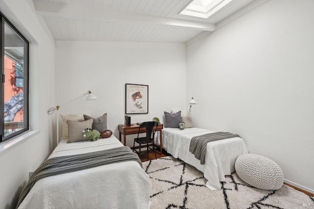 bedroom featuring a skylight, beamed ceiling, and wood finished floors