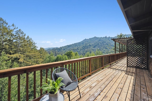 wooden terrace featuring a wooded view, a mountain view, and a pergola