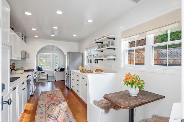 kitchen featuring arched walkways, tasteful backsplash, appliances with stainless steel finishes, white cabinets, and wood finished floors