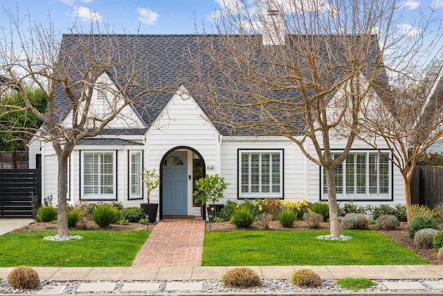 view of front of property featuring a shingled roof, a chimney, fence, and a front yard