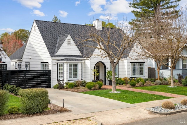 view of front of house featuring a front lawn, a chimney, a shingled roof, and fence