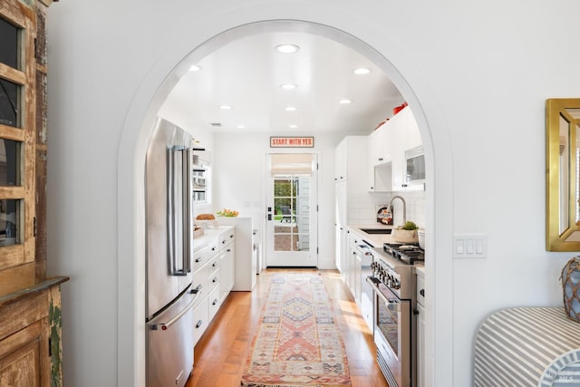 kitchen featuring high end range, a sink, light wood-type flooring, white cabinetry, and backsplash