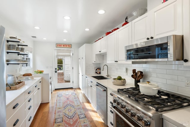 kitchen with stainless steel appliances, a sink, white cabinetry, light countertops, and light wood-type flooring