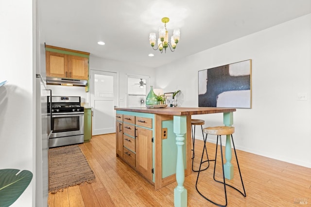 kitchen featuring light wood-style flooring, under cabinet range hood, stainless steel gas range oven, a kitchen bar, and a notable chandelier