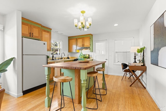 kitchen with under cabinet range hood, butcher block countertops, a kitchen breakfast bar, freestanding refrigerator, and a sink