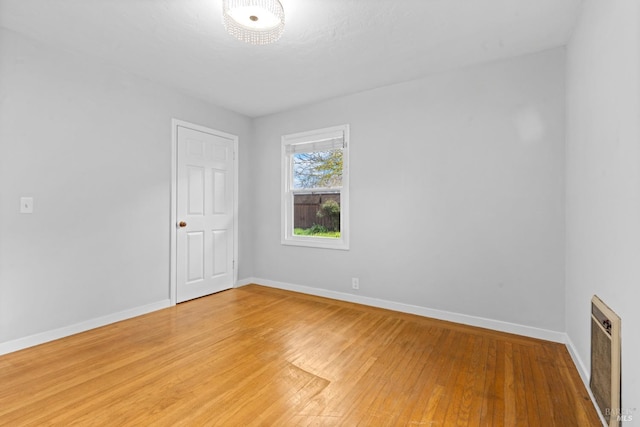 spare room featuring heating unit, baseboards, and light wood-style floors