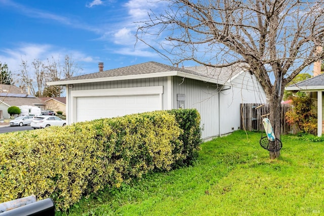 view of side of home featuring a garage, roof with shingles, a lawn, and fence