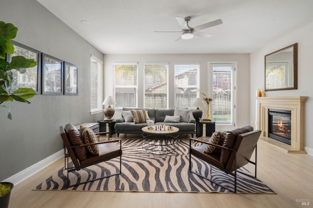 living room featuring a ceiling fan, a glass covered fireplace, baseboards, and wood finished floors