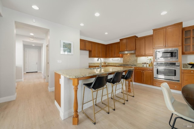 kitchen featuring under cabinet range hood, a sink, appliances with stainless steel finishes, light wood-type flooring, and brown cabinetry