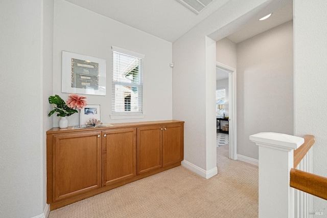 hall featuring visible vents, baseboards, and light colored carpet