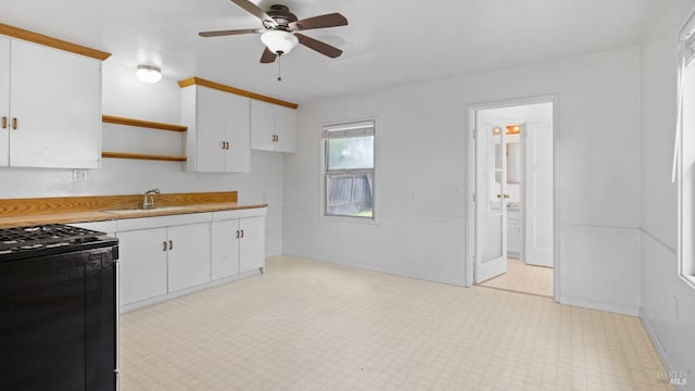 kitchen with light countertops, light floors, open shelves, a sink, and gas stove