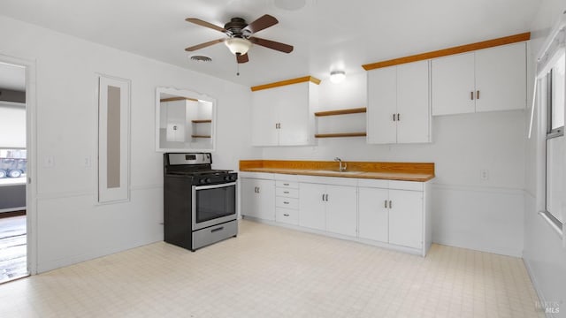 kitchen with light floors, a sink, white cabinets, stainless steel gas range, and open shelves