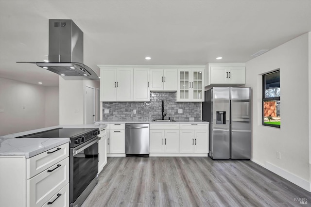 kitchen featuring light wood finished floors, stainless steel appliances, decorative backsplash, a sink, and island range hood