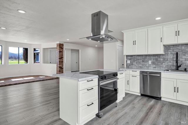 kitchen featuring light wood-style flooring, island range hood, a sink, open floor plan, and appliances with stainless steel finishes