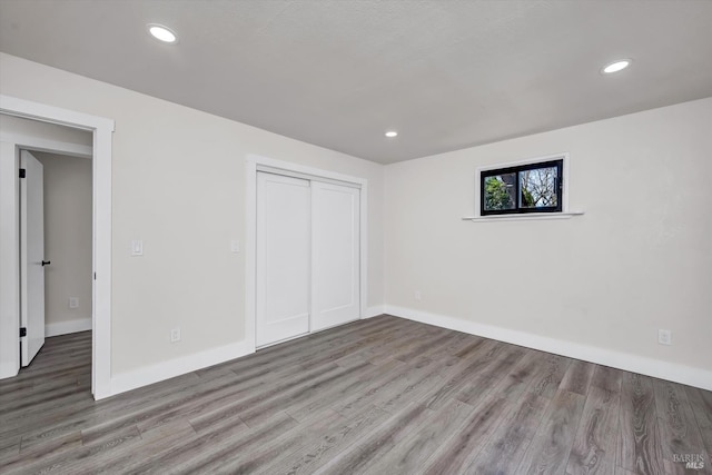 unfurnished bedroom with recessed lighting, a closet, baseboards, and wood finished floors