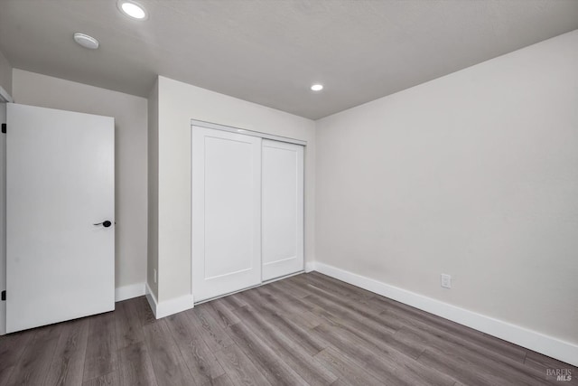 unfurnished bedroom with a closet, recessed lighting, wood finished floors, and baseboards