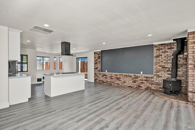 unfurnished living room featuring brick wall, a wood stove, wood finished floors, and visible vents