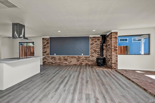 unfurnished living room with a wood stove, brick wall, visible vents, and wood finished floors