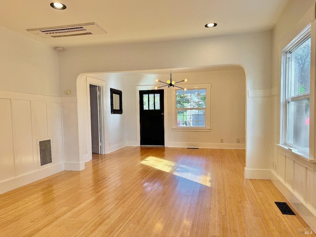 entryway with light wood finished floors, visible vents, and arched walkways