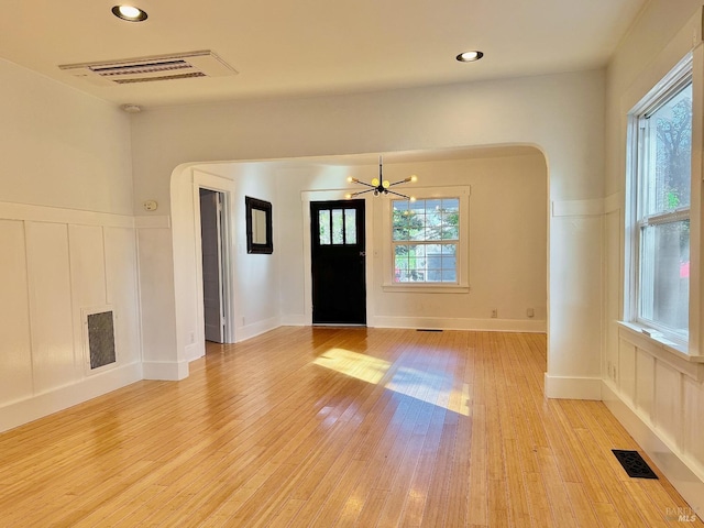 foyer entrance featuring light wood-type flooring, visible vents, arched walkways, and a decorative wall