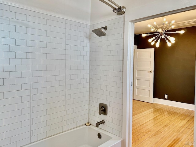 bathroom with baseboards, washtub / shower combination, wood finished floors, and a chandelier