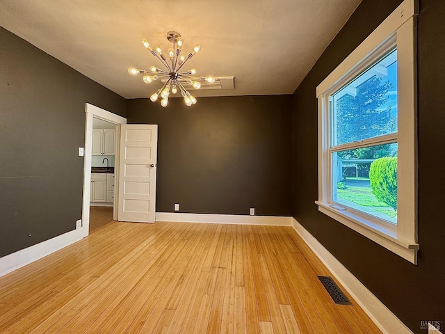 empty room featuring baseboards, light wood finished floors, visible vents, and an inviting chandelier