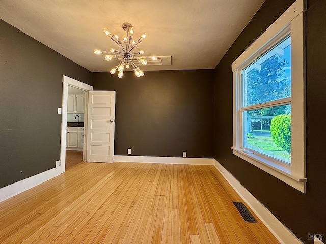 spare room with a sink, light wood-type flooring, baseboards, visible vents, and an inviting chandelier