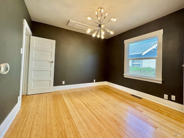 empty room with hardwood / wood-style flooring, an inviting chandelier, visible vents, and baseboards