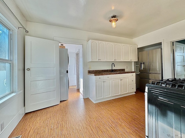 kitchen with white cabinets, high end fridge, dark countertops, a sink, and black gas stove