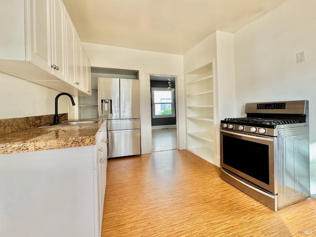 kitchen featuring a sink, built in shelves, stainless steel appliances, light wood finished floors, and white cabinets