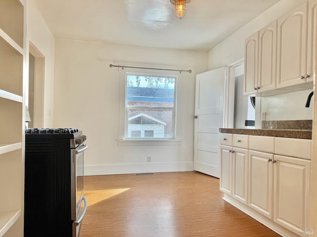 kitchen featuring dark countertops, visible vents, light wood-style flooring, stainless steel gas range oven, and baseboards