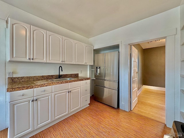 kitchen featuring tile counters, light wood-style flooring, white cabinets, a sink, and stainless steel fridge