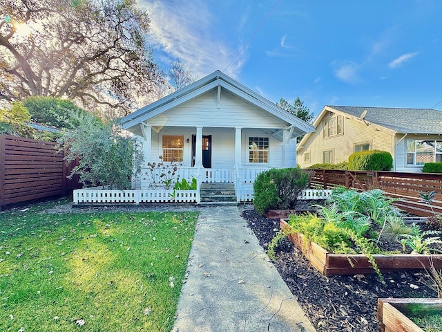 bungalow-style home with a porch, a front yard, fence, and a garden