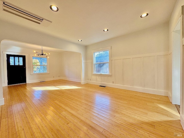 interior space with light wood finished floors, a wainscoted wall, an inviting chandelier, visible vents, and a decorative wall