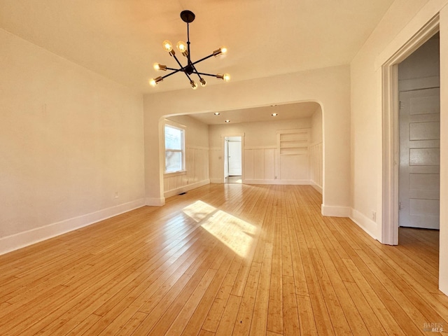 empty room featuring arched walkways, light wood-style flooring, baseboards, and an inviting chandelier