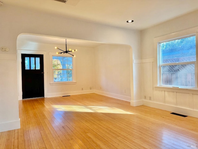 entryway with light wood finished floors, arched walkways, plenty of natural light, visible vents, and an inviting chandelier