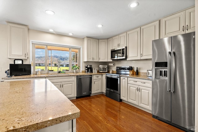 kitchen with recessed lighting, stainless steel appliances, wood finished floors, a sink, and light stone countertops