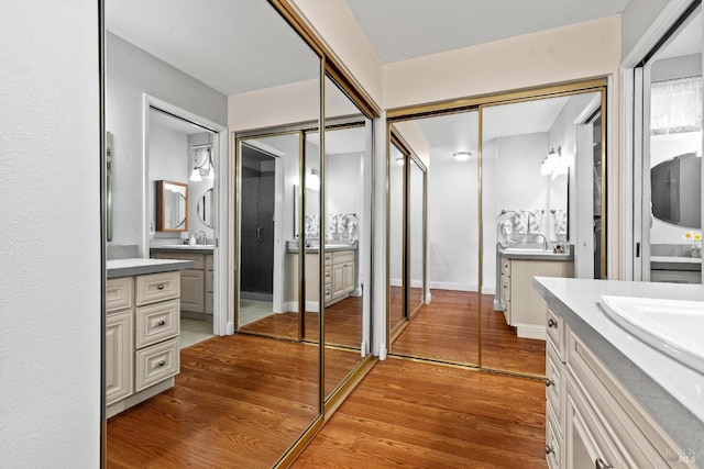 bathroom with a sink, baseboards, two vanities, and wood finished floors