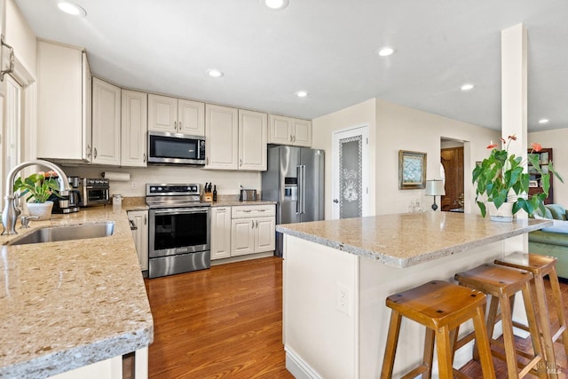 kitchen featuring stainless steel appliances, recessed lighting, a sink, wood finished floors, and a kitchen bar