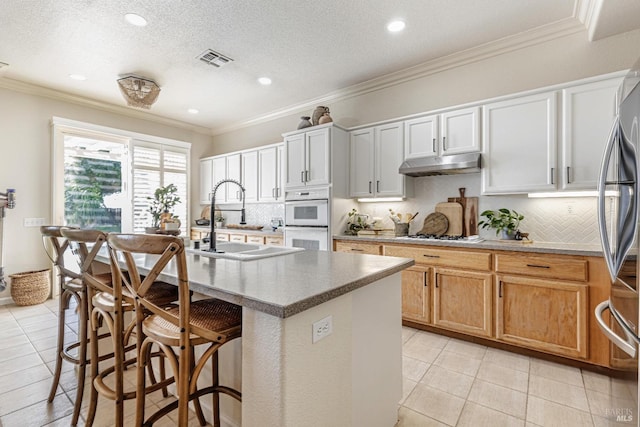 kitchen with visible vents, double oven, ornamental molding, a sink, and under cabinet range hood