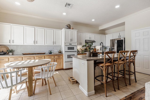 kitchen featuring stainless steel fridge, visible vents, decorative backsplash, white double oven, and a breakfast bar area