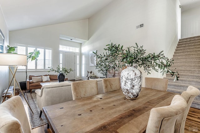 dining area featuring high vaulted ceiling, visible vents, and stairway