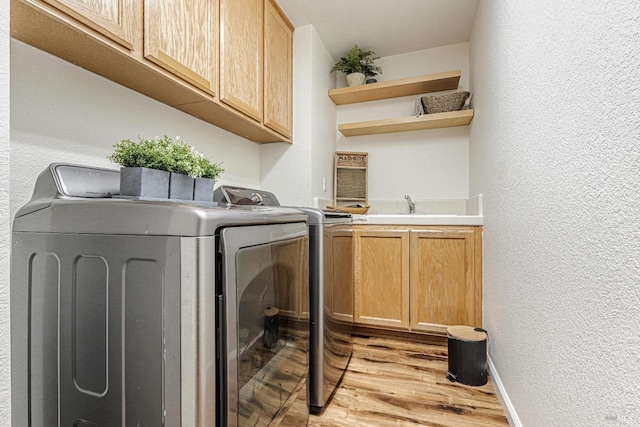 clothes washing area featuring cabinet space, baseboards, a textured wall, light wood-style flooring, and washer and dryer